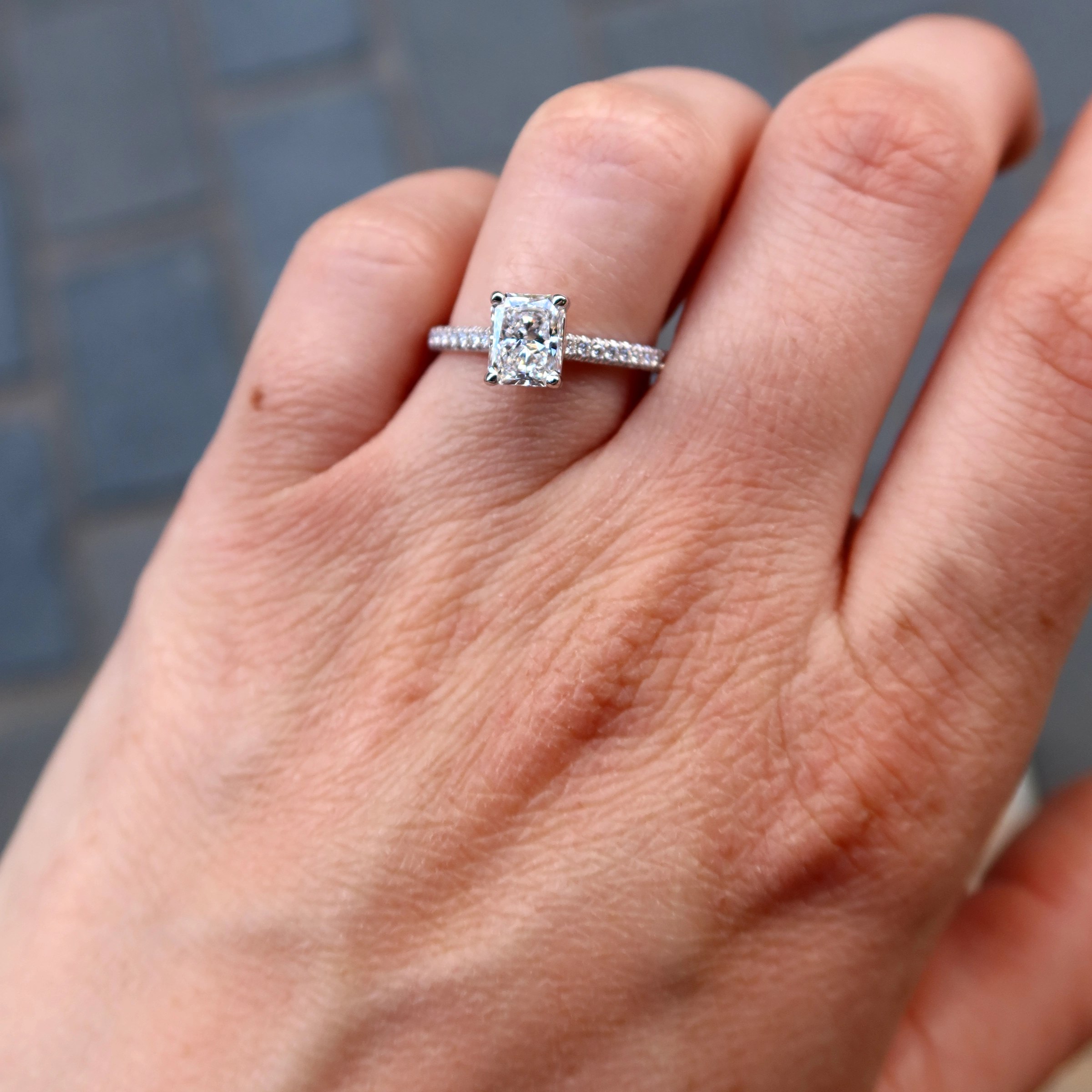 1.02 Ct Radiant Cut Diamant Ring In 18K Witgoud Met Gia Diamant 2 - Orogem Jewelers Handfoto Van Een 1.02 Ct Radiant Cut Diamant Ring In 18K Witgoud Met Gia-Gecertificeerde Middendiamant En Diamantgezette Band.