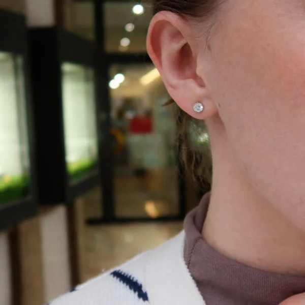 Orecchini punto luce 1 carato indossati all’orecchio con diamanti naturali rotondi E SI1 certificati GIA in oro bianco 18 carati.