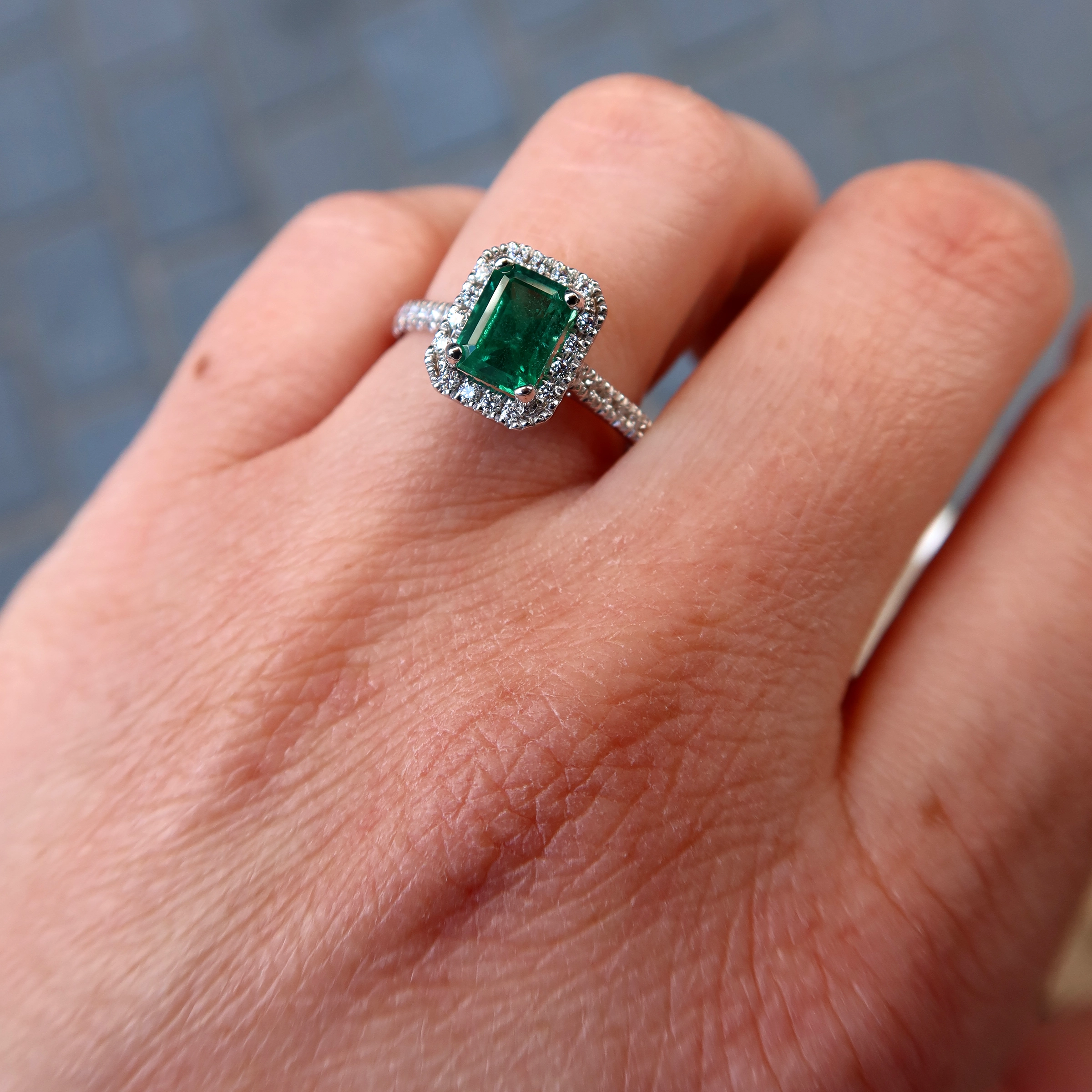 Bague Halo Émeraude Taille Émeraude En Or Blanc 18 Carats 4 - Orogem Jewelers Gros Plan Porté D’une Bague Halo Émeraude Taille Émeraude En Or Blanc 18 Carats Avec 0,25 Ct De Diamants Naturels.