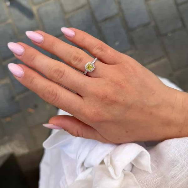 Fancy intense yellow diamond halo ring worn on the hand with cushion yellow diamond center and diamond-set white gold band.