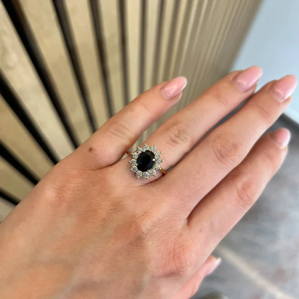 Yellow gold sapphire diamond ring worn on the hand with a 2.14 ct oval sapphire and surrounding natural diamonds.