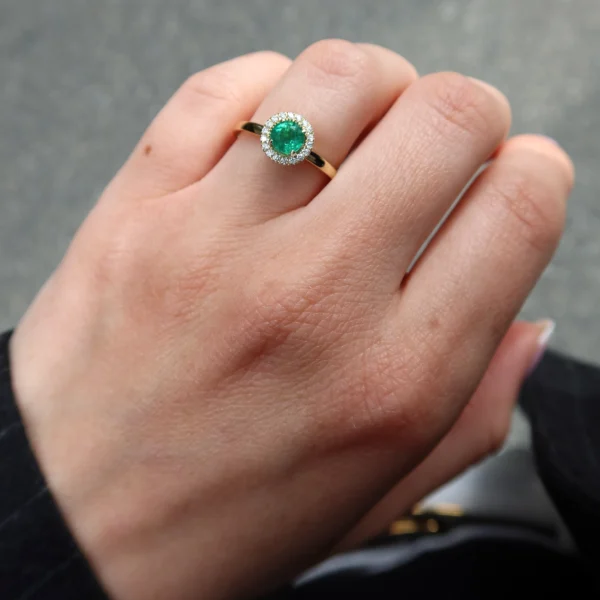 Elegante anello halo in oro giallo 18K con smeraldo naturale rotondo da 0,54 carati circondato da 0,10 carati di diamanti naturali D–F VS, che unisce colore vibrante e raffinatezza senza tempo