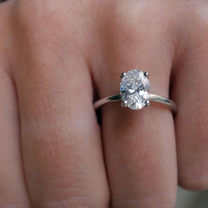1.51 Carat Oval Cut Diamond Solitaire Engagement Ring In 18K White Gold, Shown At An Angle On The Hand.