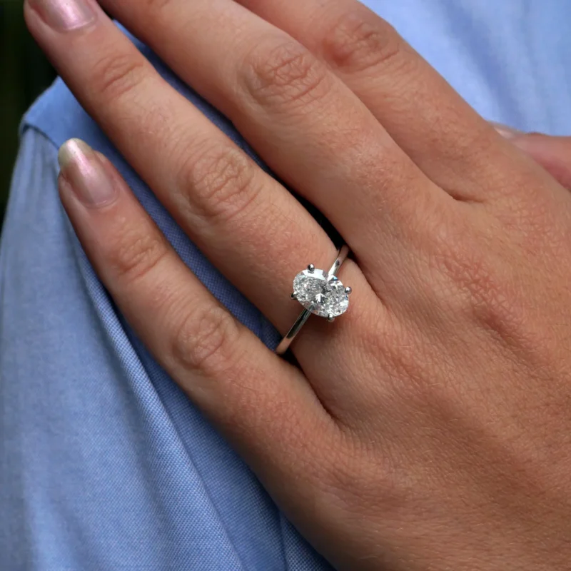 Oval Cut Diamond Solitaire Engagement Ring, 1.51 Carats, In 18K White Gold, Displayed On Finger With A Blue Shirt Sleeve.