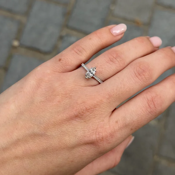 Close-up van een 18K witgouden ring met marquise diamant en pavé diamanten in de band, gedragen aan de hand buiten.