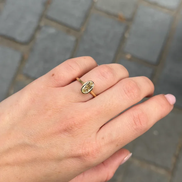 Hand met een 1.00 ct ovale step cut Y-Z VS2 GIA diamanten ring in gepolijst 18K geel goud.