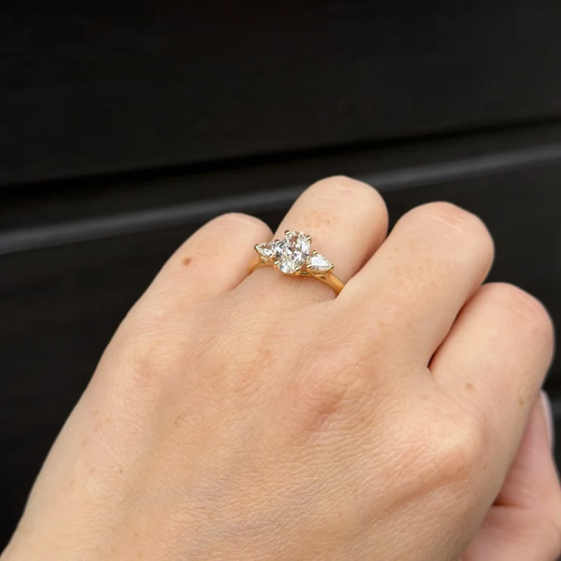 Anello Trilogy Con Diamante Ovale 1.04 Ct G Vs1 Gia E 0.28 Ct Taglio Pera In Oro Giallo 18K 2 - Orogem Jewelers Side Angle Of 18K Yellow Gold Ring Featuring 1.04 Ct Oval Gia Diamond And Pear Side Stones, Worn On Hand.
