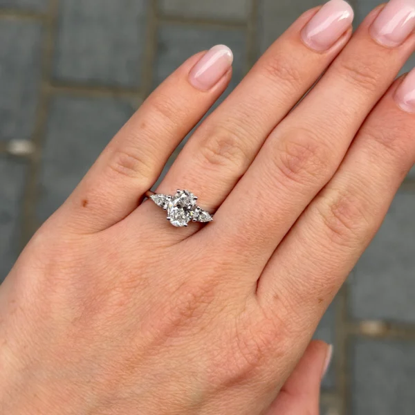 Hand met 18K witgouden ring met ovale diamant 1.50 ct GIA en peervormige zijdiamanten.