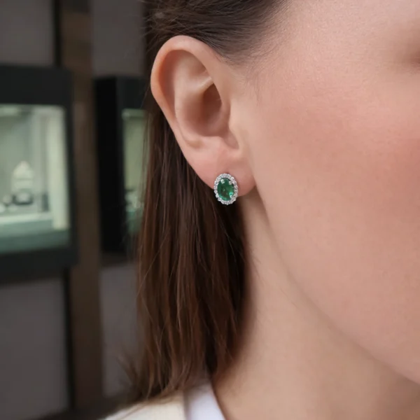 Orecchino halo con smeraldo ovale indossato in oro bianco 18k con centro verde intenso e contorno di diamanti brillanti.