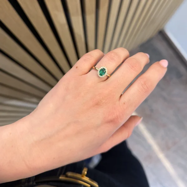 Emerald halo ring with diamond accents worn on the hand in yellow gold