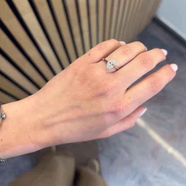 Bague diamant de synthèse ovale portée à la main en or blanc 18 carats avec halo caché sous la pierre centrale.