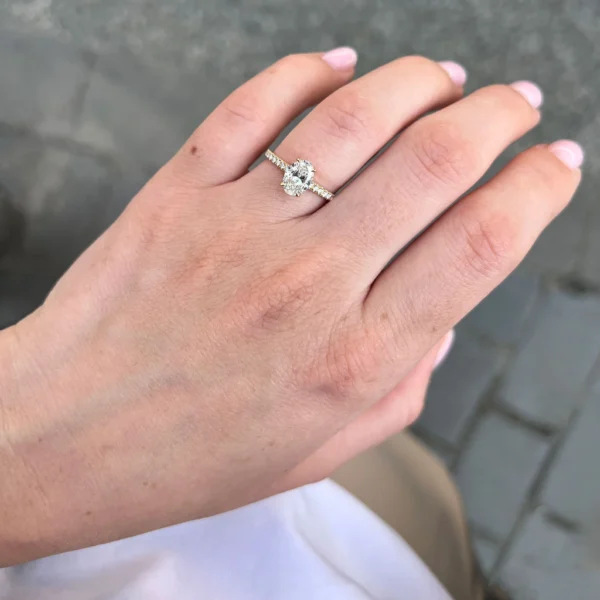 Handfoto van een 18k geelgouden ring met een ovale D VS1 lab-grown diamant van 1.00 ct en verfijnde pavé gezette diamanten op de band.