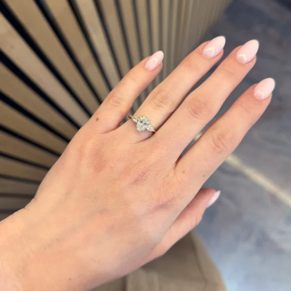 Bague diamant de synthèse ovale or jaune 18 carats portée à la main avec diamants latéraux taille poire.
