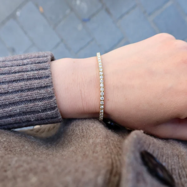 Bracelet tennis diamants or jaune porté au poignet en or jaune 18 carats avec une rangée délicate de diamants naturels.
