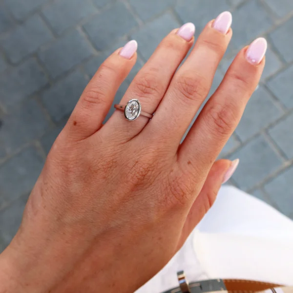 Oval step cut bezel diamond ring worn on the hand in 18k white gold with elongated bezel-set center diamond.