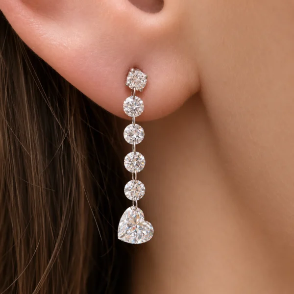 White gold heart diamond drop earrings worn on the ear with five round diamonds above a suspended heart cut diamond.