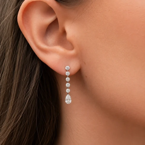 Boucle pendante diamants poire en or blanc 18 carats portée à l’oreille avec cinq diamants ronds brillants au-dessus d’un diamant poire suspendu.