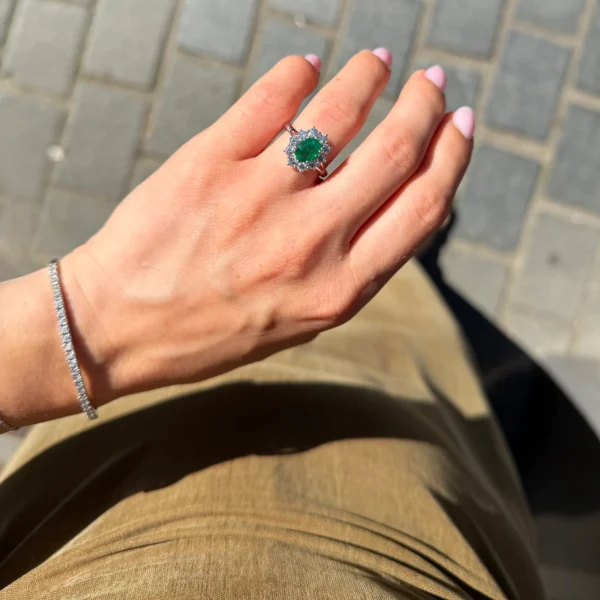 Oval emerald halo ring worn on the hand in 18k white gold with vivid green center stone and diamond halo.