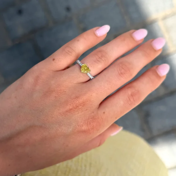 Fancy yellow heart diamond ring worn on the hand in 18k white and yellow gold with a heart cut yellow center diamond and diamond band.