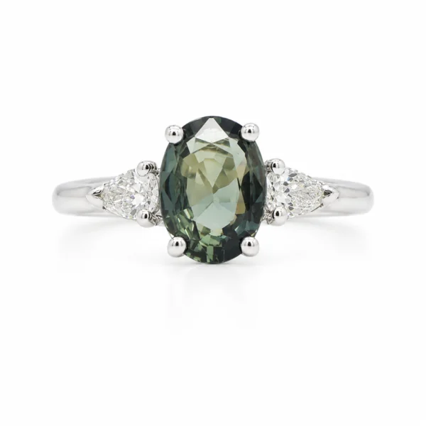 Green sapphire three stone engagement ring in 18k white gold with a 1.05 ct oval green sapphire and 0.21 ct pear cut D-F VS diamonds.