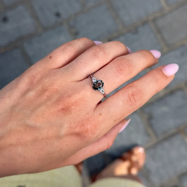 Oval green sapphire and pear diamond three-stone ring worn on the hand in polished 18k white gold.