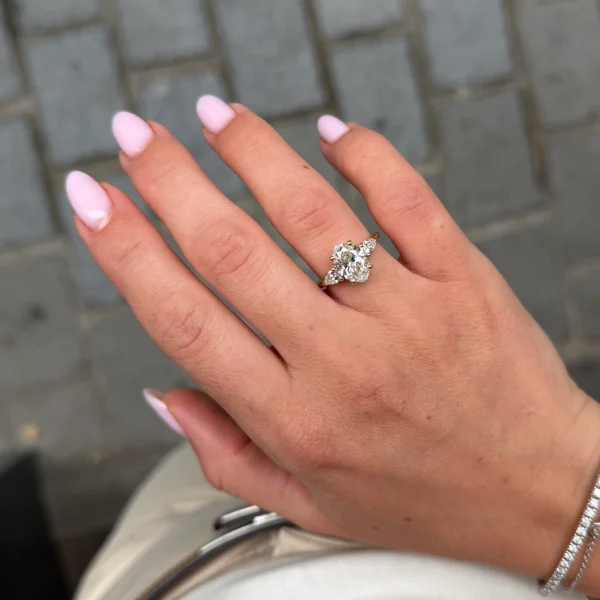 Bague trois diamants ovale portée à la main avec grand diamant central ovale et diamants latéraux taille poire.