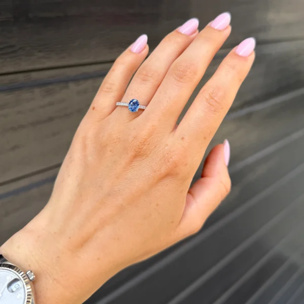 Oval sapphire engagement ring worn on the hand with a vivid blue center stone and diamond-set white gold band.