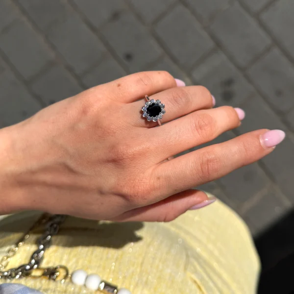 Oval sapphire floral halo ring worn on the hand with a deep blue center stone and round brilliant diamond surround.
