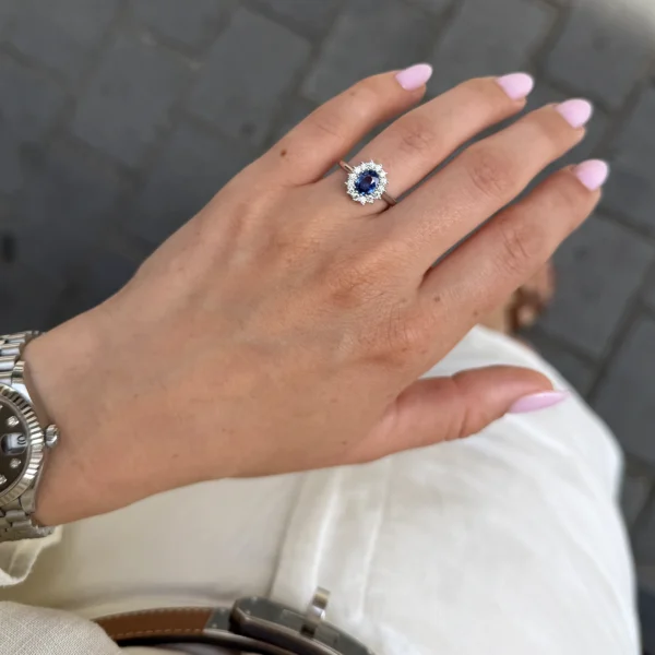 Bague halo saphir ovale portée à la main avec pierre centrale bleu intense et entourage lumineux de diamants.