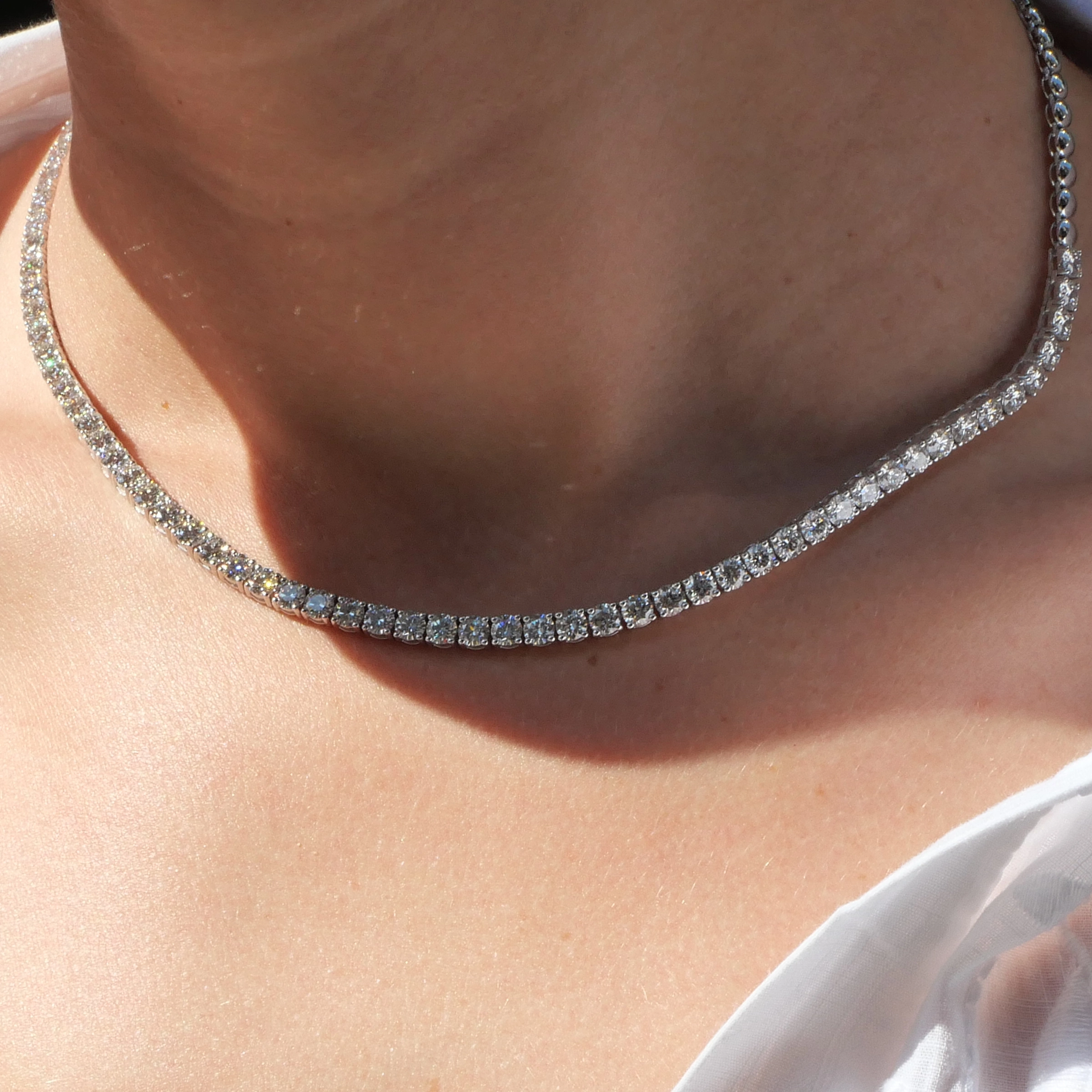 11.40 Ct Gia Diamond Tennis Necklace 43 Cm 4 2 Schuin Aanzicht Van De Ketting Van 43 Cm Op Het Sleutelbeen, Waarbij De Diamanten Lijn Overgaat In Gepolijste Witgouden Kralen.