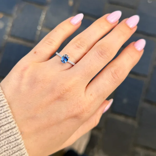 0,91 Ct Blauwe Ovale Saffier In Vier Klauwen Op Een Pavé Band In 18K Witgoud, Gedragen Aan De Hand